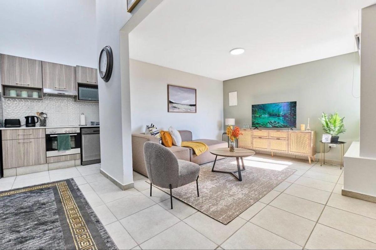 A bright open-plan living area featuring a modern kitchen with wood-finish cabinetry and tiled flooring, seamlessly flowing into a comfortable lounge space.