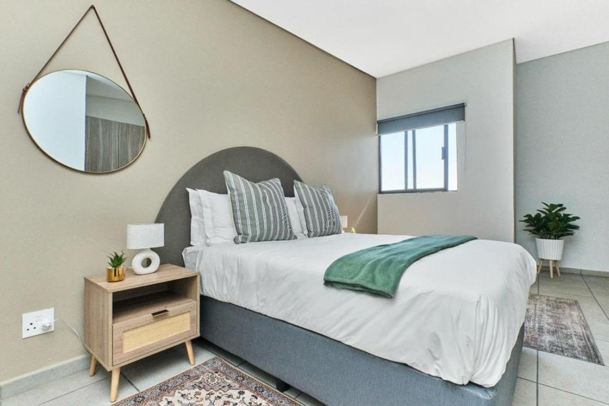 A well-maintained bedroom featuring neutral wall tones, tiled flooring, and a functional sliding window with a roller blind.