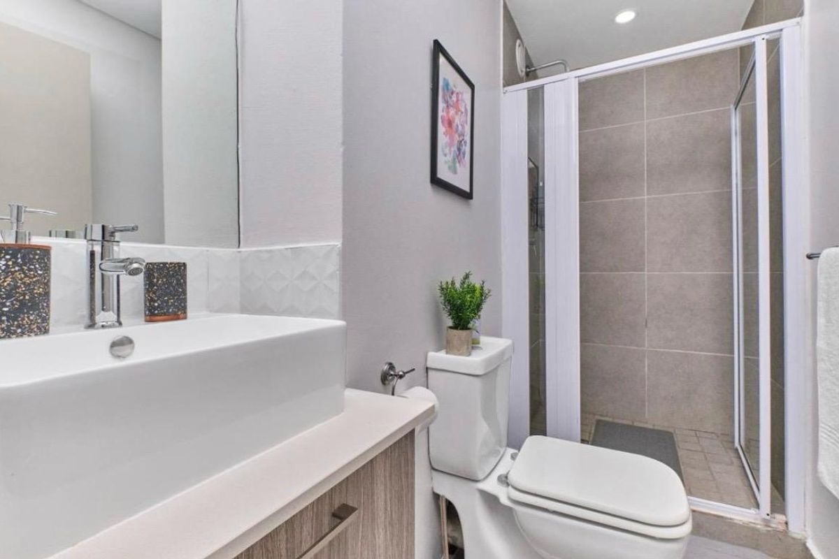 Modern bathroom featuring a vanity with vessel sink, chrome fixtures, a white toilet, and a glass-enclosed shower with neutral wall tiling.