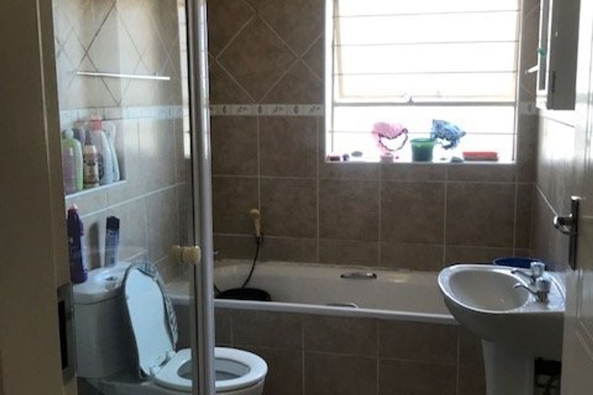 A dated bathroom featuring a pedestal basin, bathtub, and separate shower enclosure with tiled finishes, showing signs of ceiling water damage.