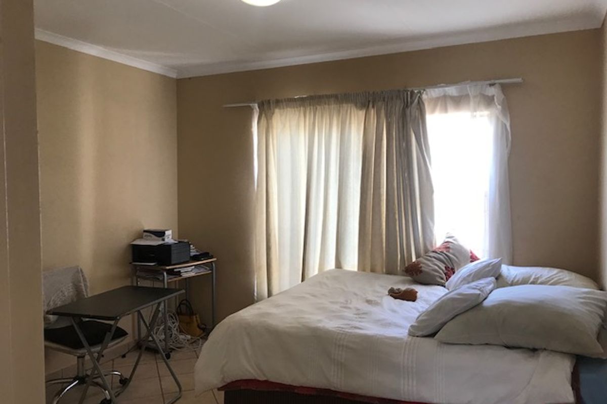 A standard bedroom featuring tiled flooring, neutral wall paint, and a window with curtain fittings.