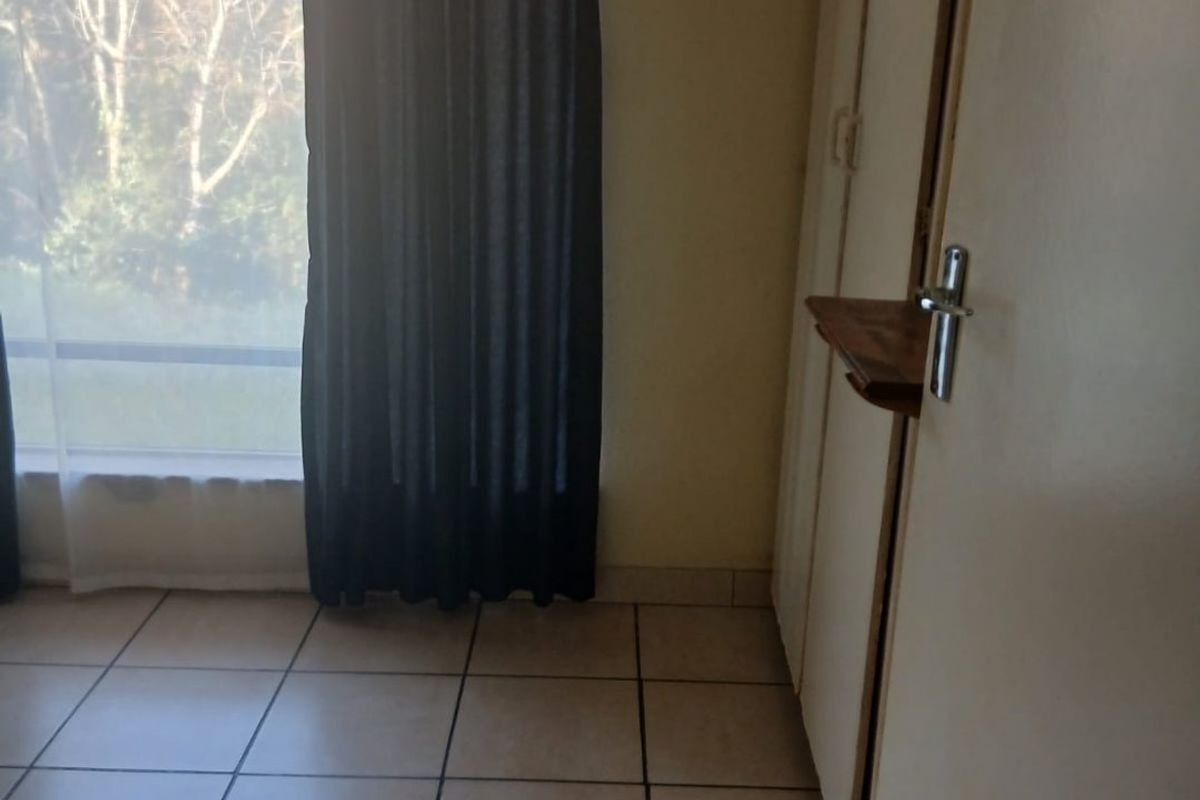 A vacant bedroom featuring tiled flooring, built-in cupboards, and a large window providing natural light.
