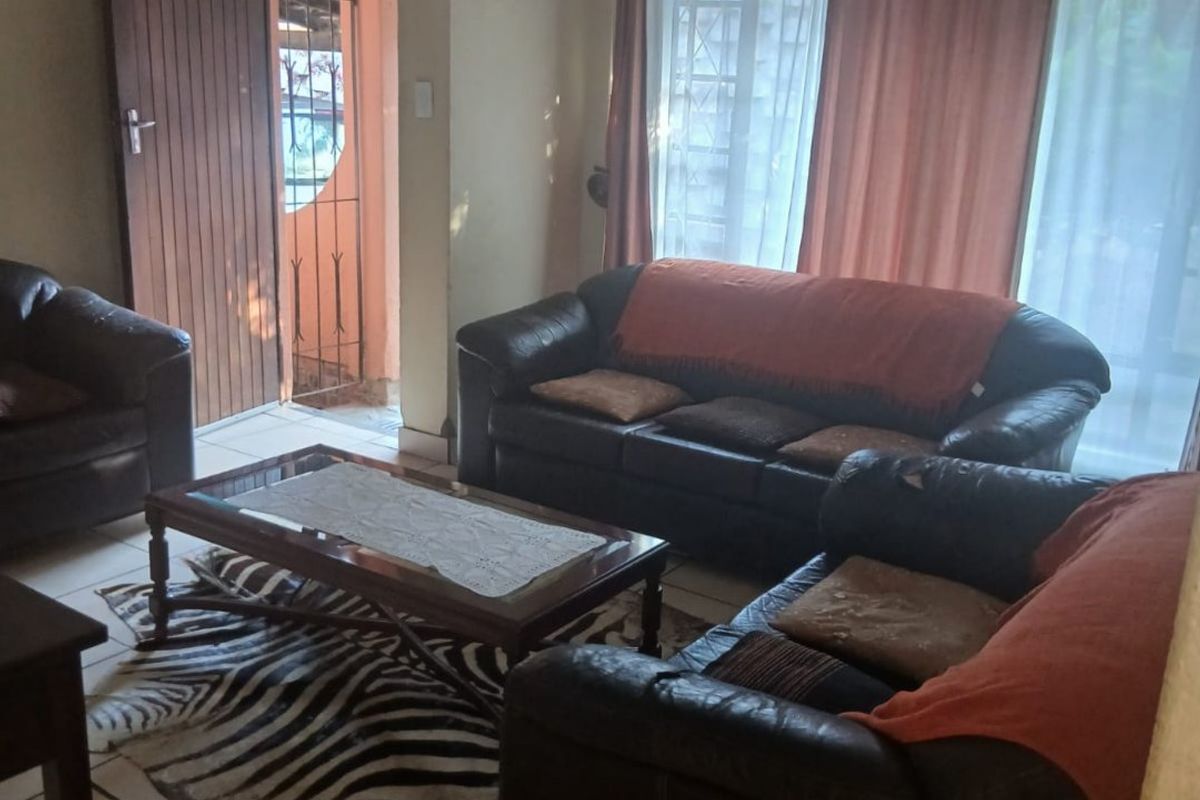 A living room featuring tiled flooring and a ceiling fan, with direct access to an exterior entrance area through a security gate.