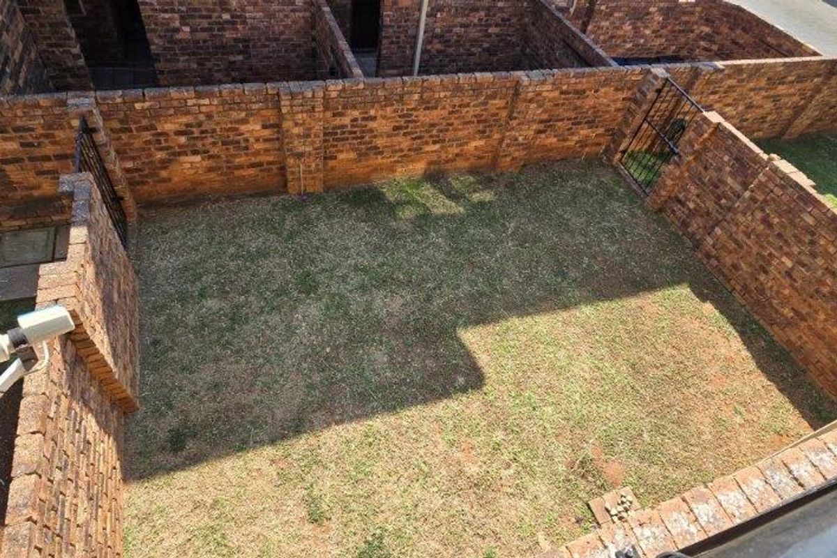 A private rear garden area enclosed by brick boundary walls, featuring a lawn and a mounted security camera.