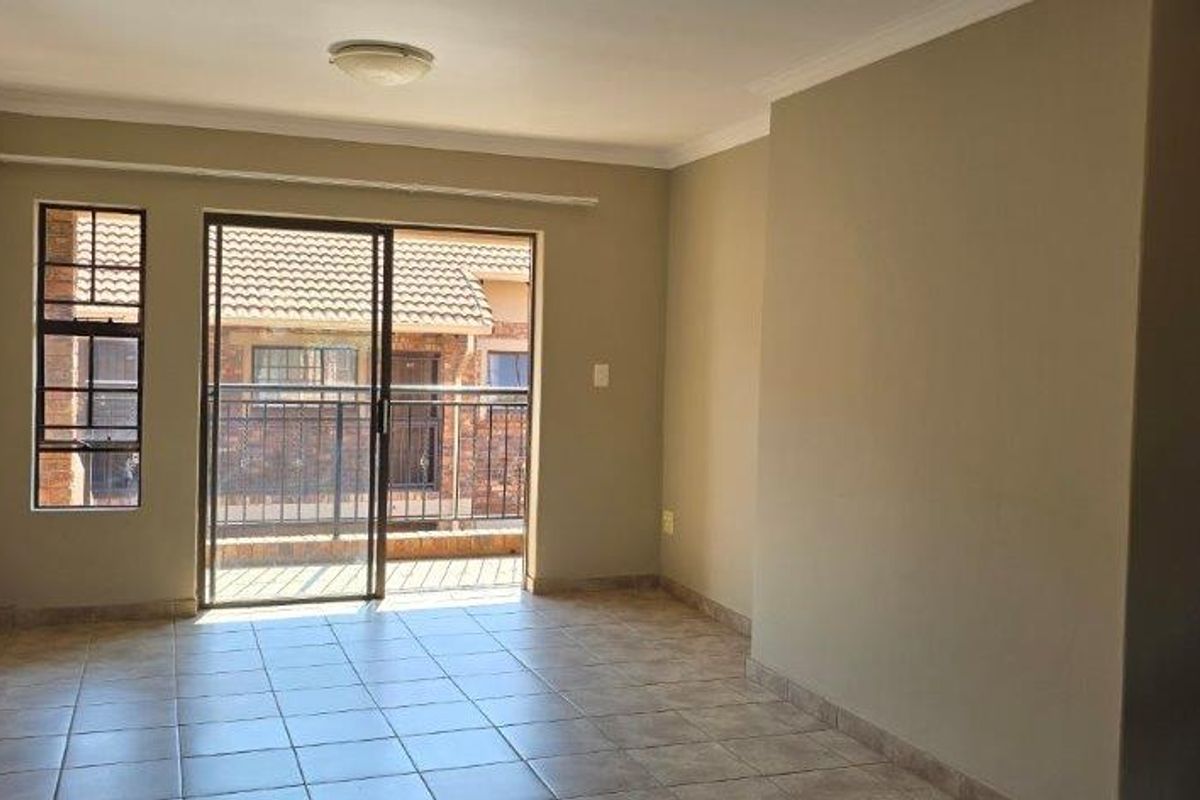 An empty, neutrally painted living room featuring tiled flooring and a sliding glass door that opens onto a balcony.