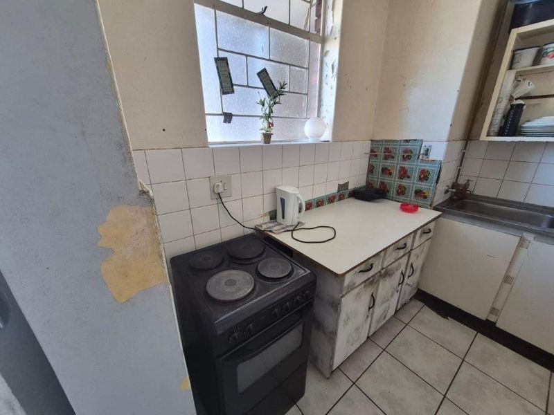 A compact kitchen featuring a freestanding electric stove, tiled backsplash, and built-in cabinetry, currently requiring significant cosmetic renovation and surface repairs.