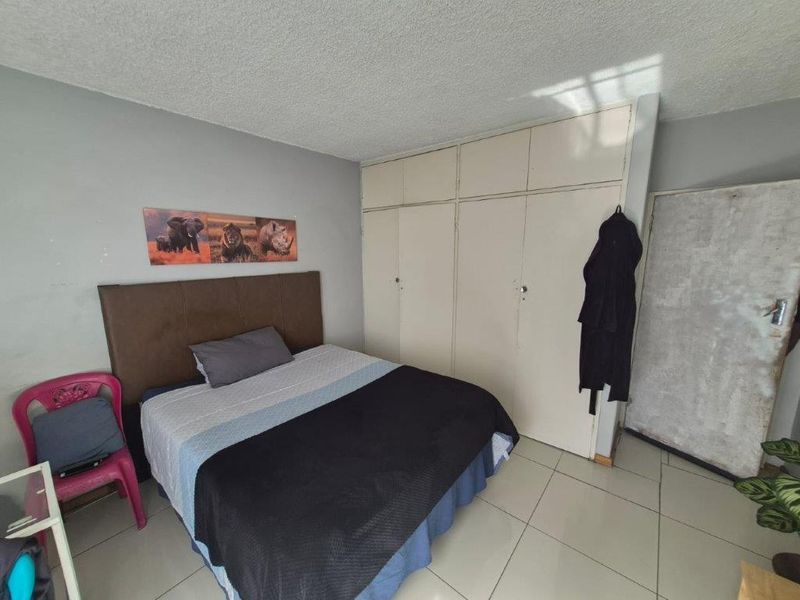 A bedroom featuring tiled flooring and built-in cupboards, offering a functional space with potential for cosmetic updates.