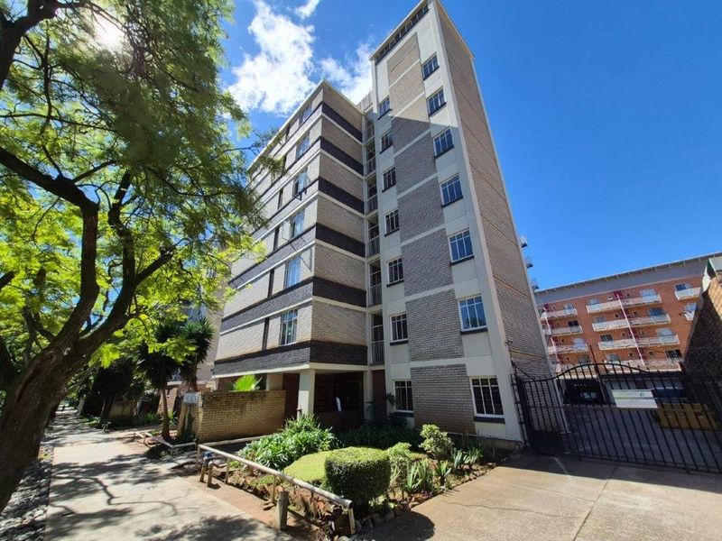 Exterior view of a multi-story apartment building featuring a brick facade, secure gated entrance, and established garden area.