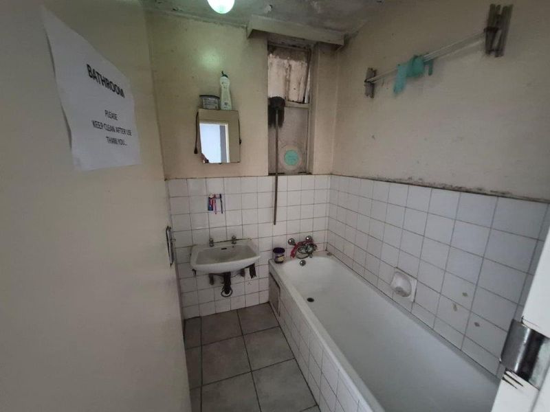 A dated bathroom featuring a standard bathtub and wall-mounted basin, requiring significant renovation and cosmetic updates to improve its condition and functionality.
