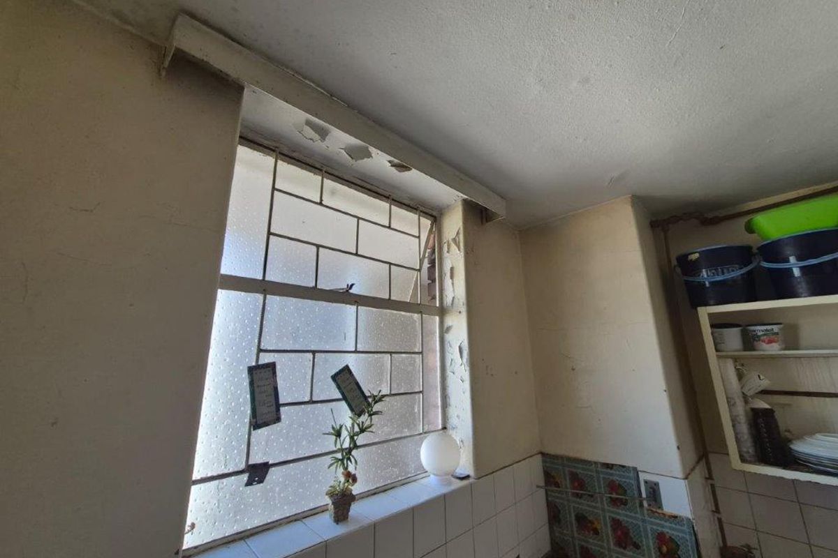 A kitchen area showing significant signs of wear, including peeling paint and damaged plaster around the window frame, requiring maintenance and cosmetic updates.