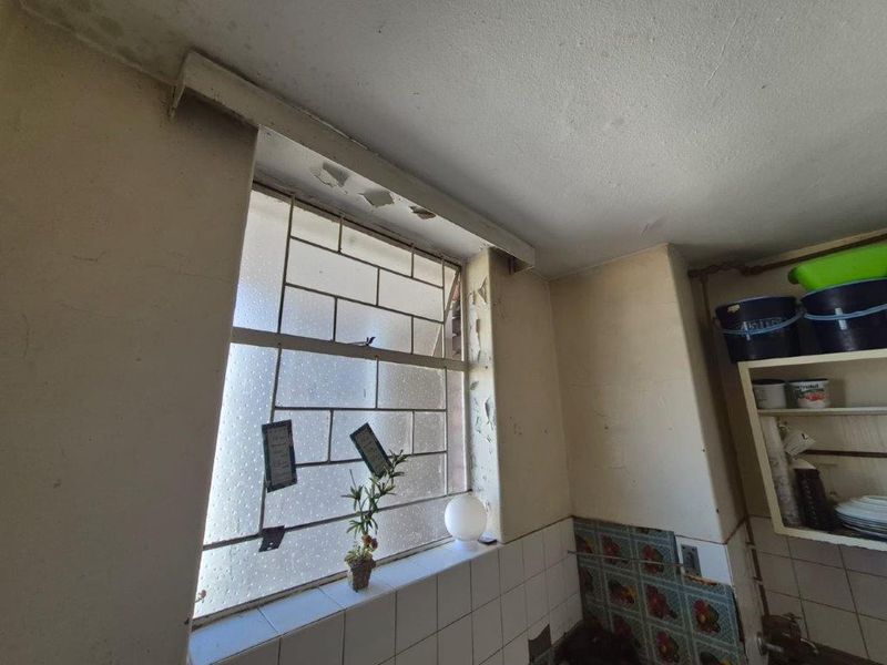 A kitchen area showing significant signs of wear, including peeling paint and damaged plaster around the window frame, requiring maintenance and cosmetic updates.