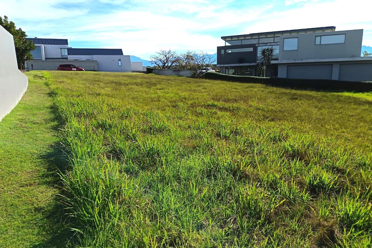 A vacant residential plot featuring a grass lawn, situated within an established neighborhood with surrounding modern residential properties.