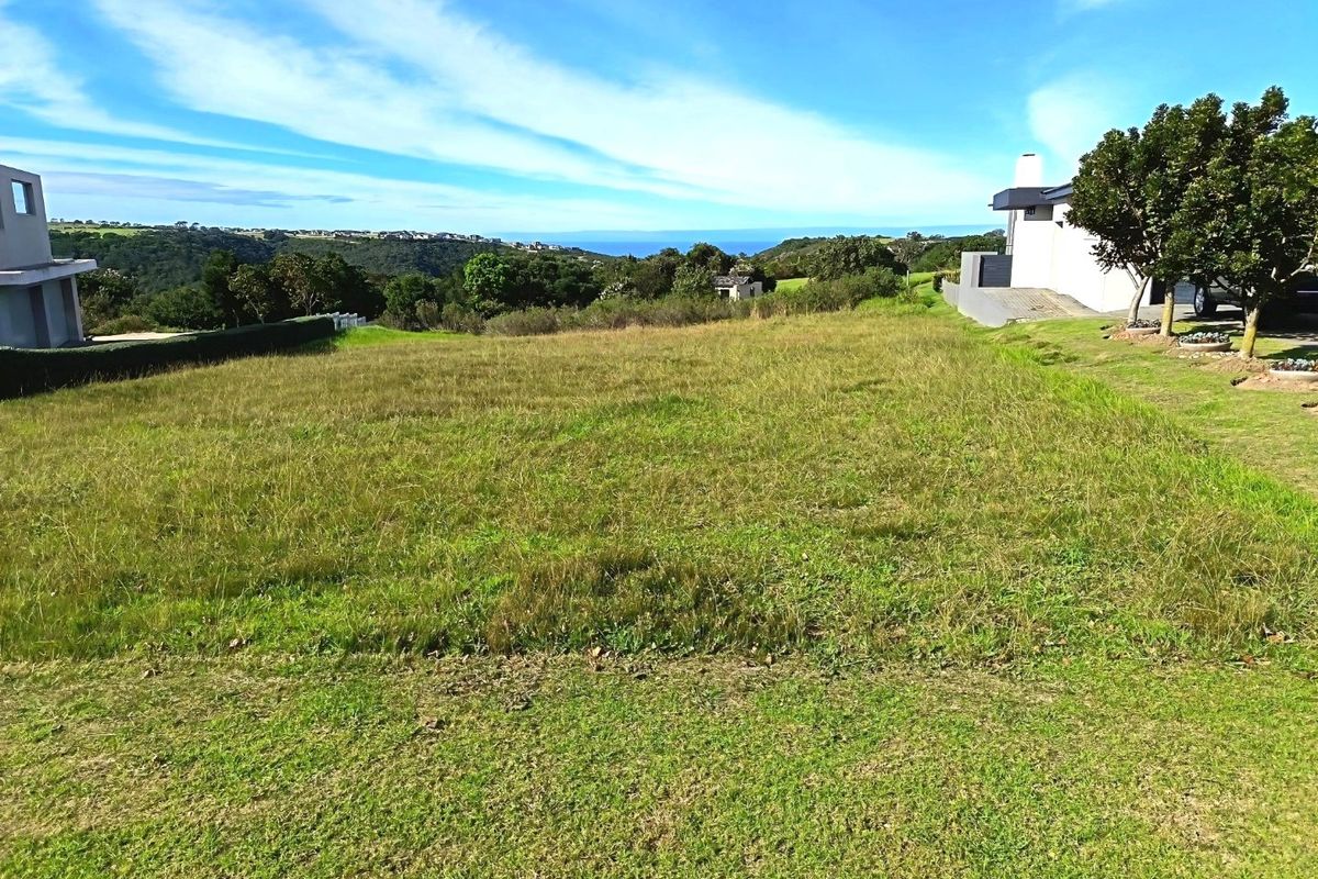 A wide-angle view of a vacant residential plot featuring natural grassland with distant coastal and landscape views.
