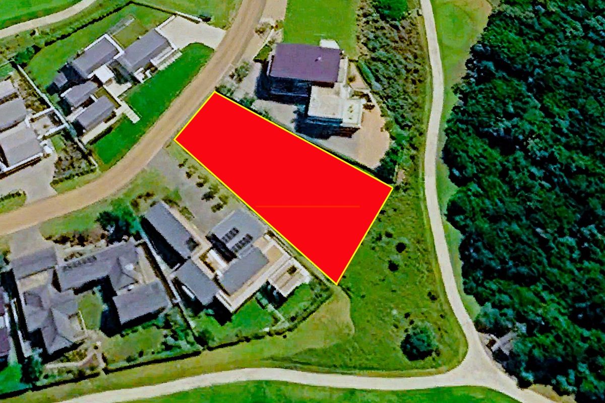 An aerial view highlighting a vacant residential land parcel situated within a developed estate, bordered by existing homes and natural vegetation.