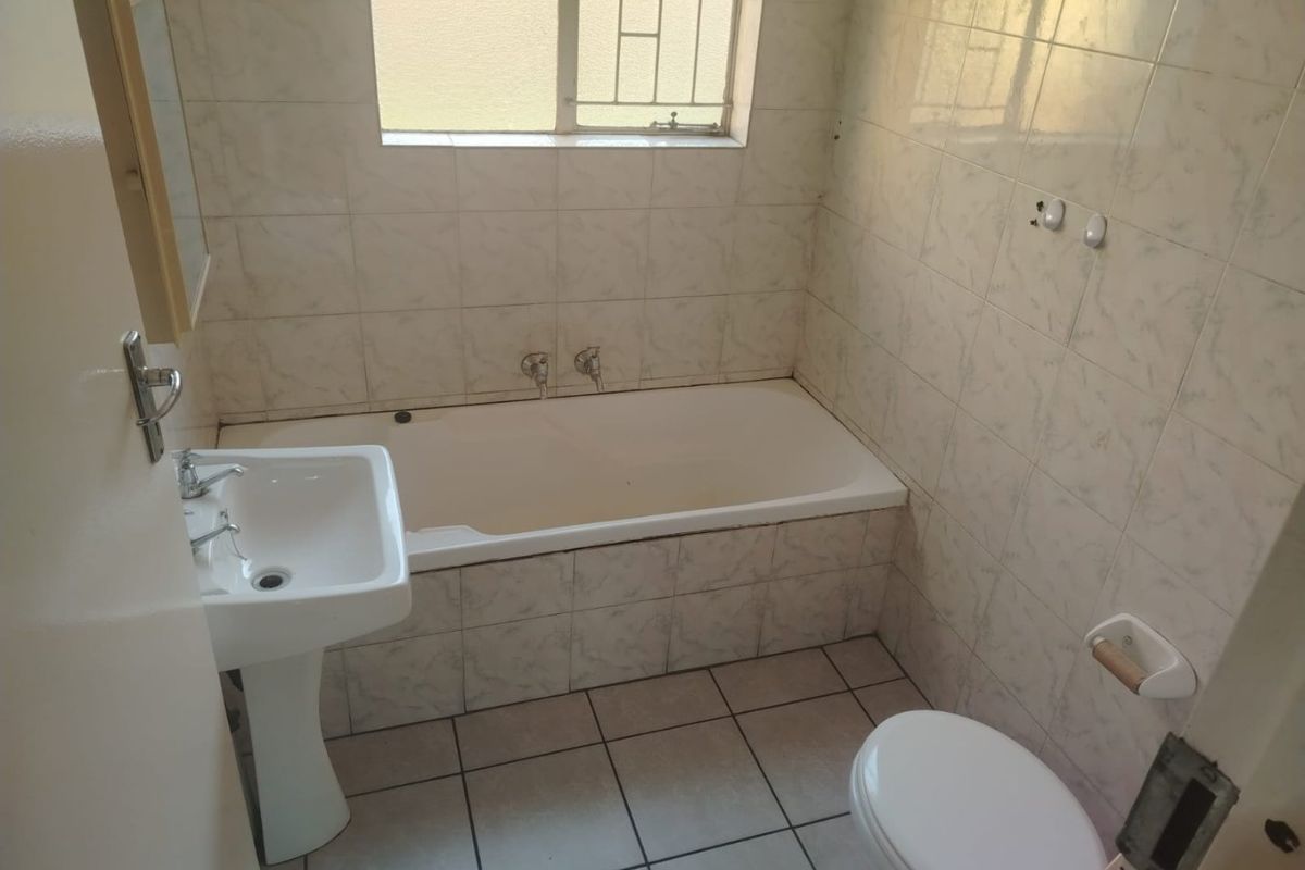 A functional bathroom featuring a pedestal basin, built-in bathtub, and tiled finishes. The space is ready for modernization and cosmetic updates.