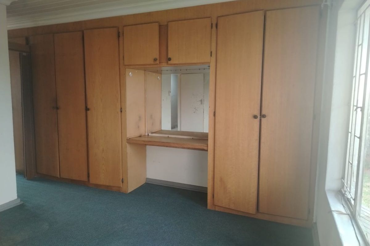 A bedroom featuring extensive built-in wooden cabinetry with an integrated vanity desk and mirror, finished with carpet flooring and a timber ceiling.