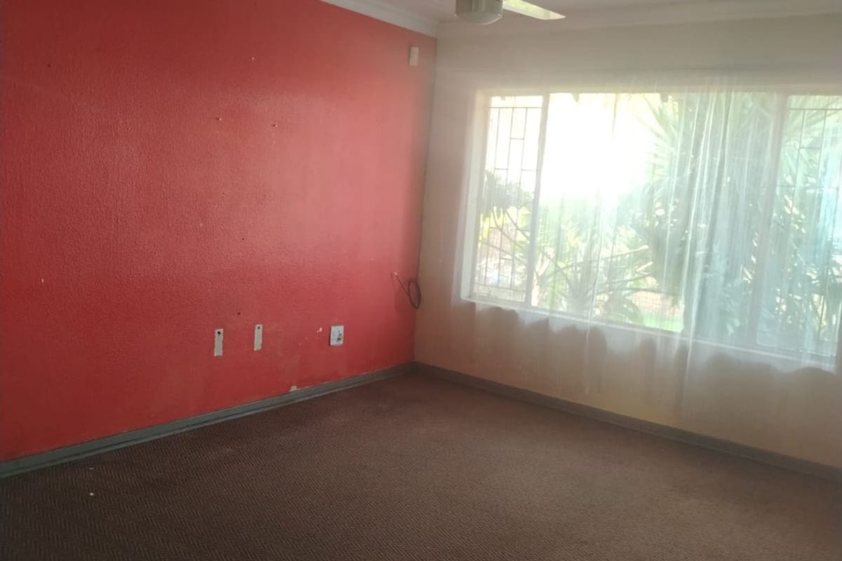 An empty living room featuring a ceiling fan, carpeted flooring, and a large window with security bars.