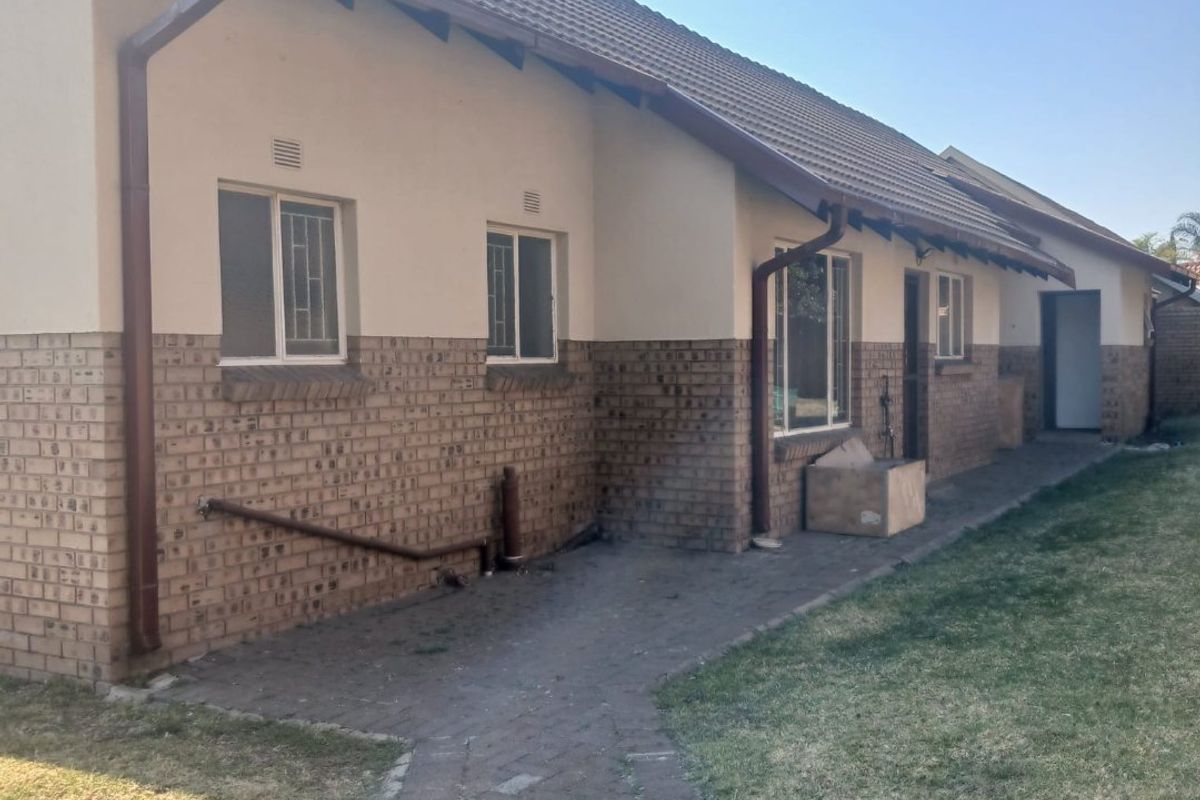 Rear view of the house featuring a brick and plaster facade, tiled roof, and a paved walkway leading along the side of the property.