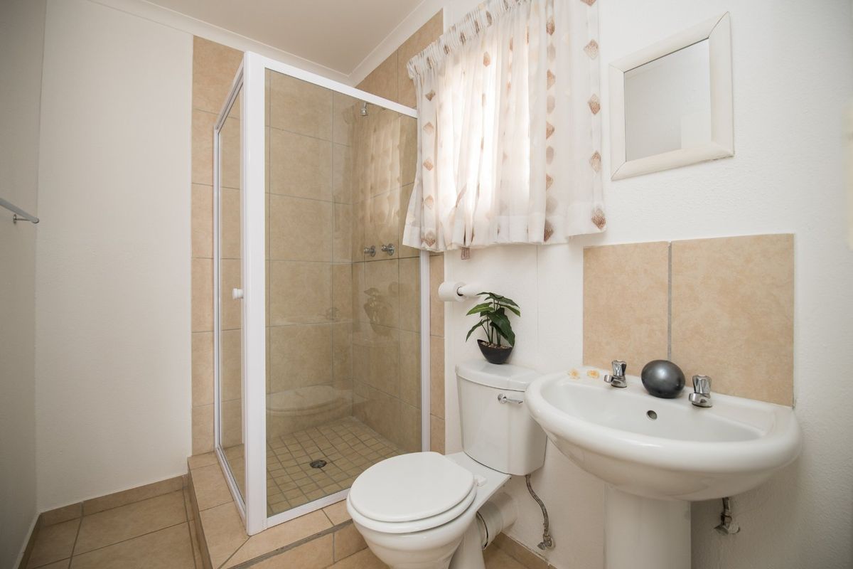 A functional bathroom featuring a shower enclosure, pedestal basin, and toilet with neutral wall and floor tiling.