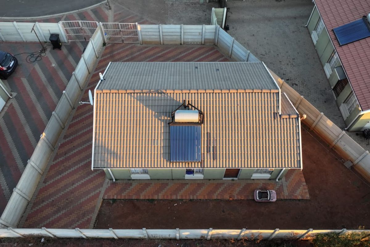 Aerial view of a residential property featuring a tiled roof with an integrated solar water heating system and a paved driveway.