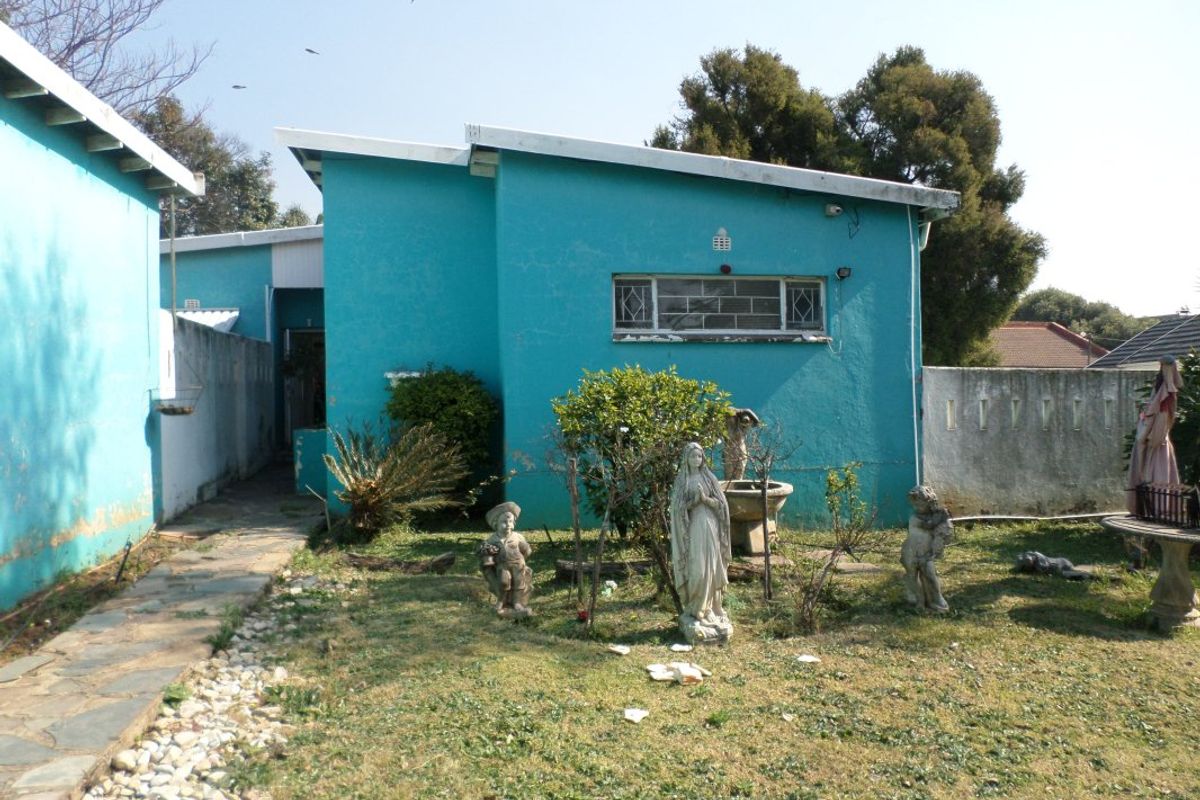Rear exterior view of the property featuring a stone pathway, garden area, and boundary wall with visible wear to the exterior paintwork.