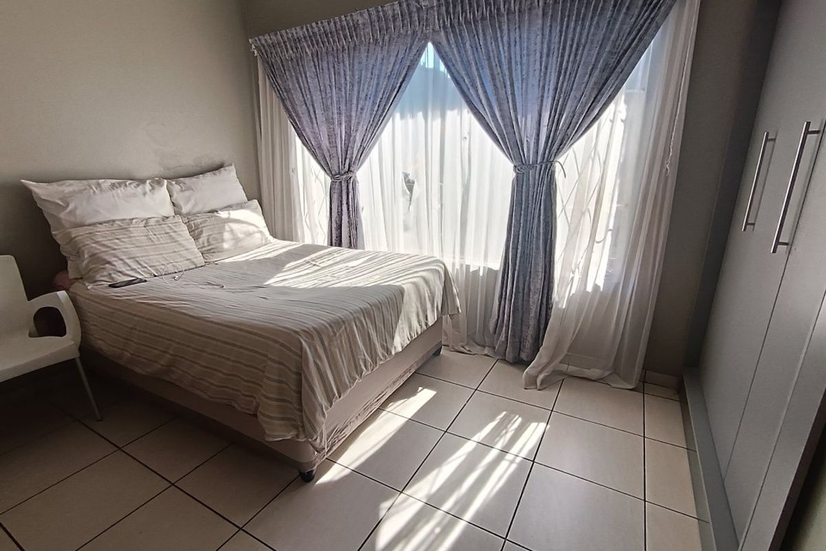 A bedroom featuring tiled flooring, built-in cupboards, and a window fitted with a security gate and curtains.