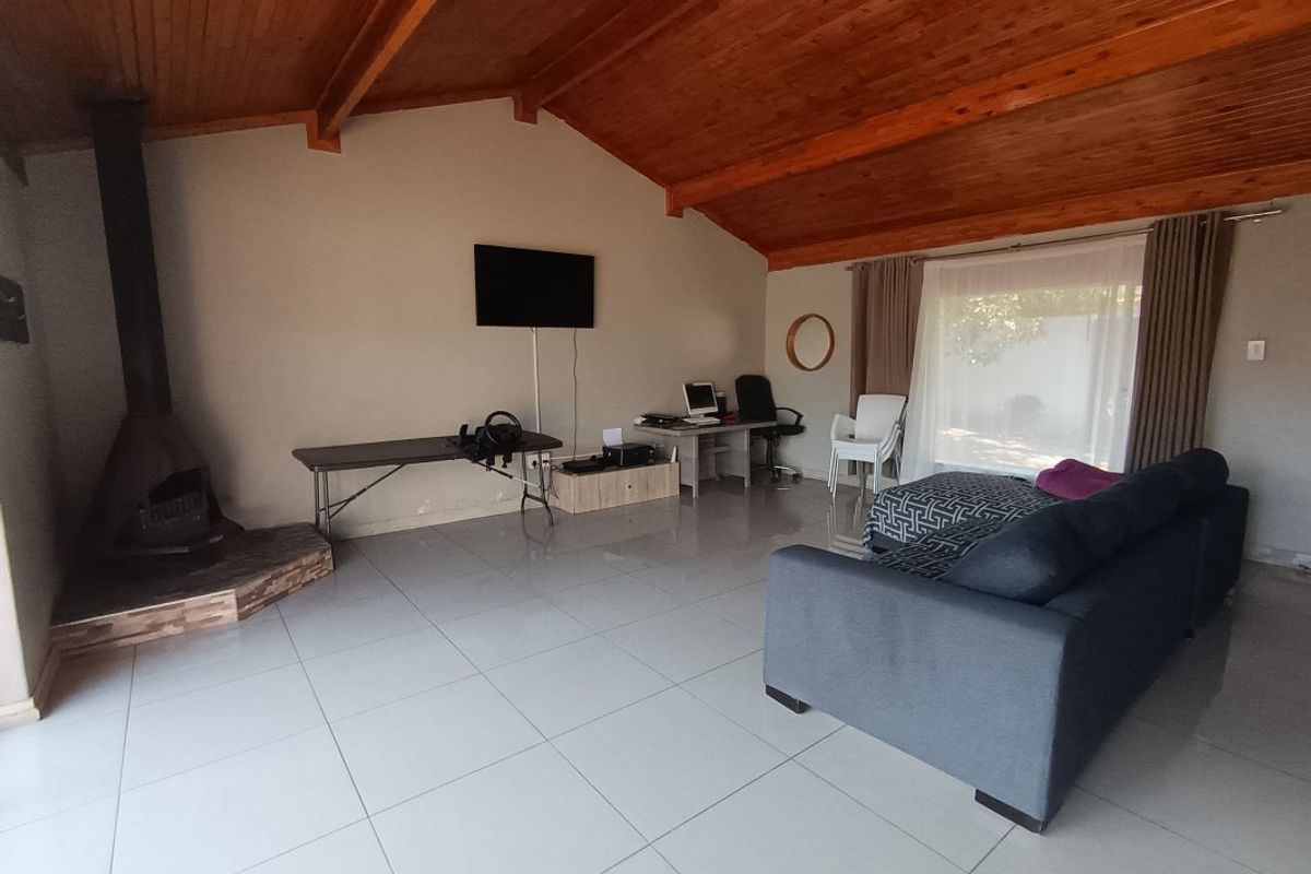 Spacious living room featuring a vaulted timber ceiling, tiled flooring, and a freestanding fireplace, offering a comfortable and versatile living space.