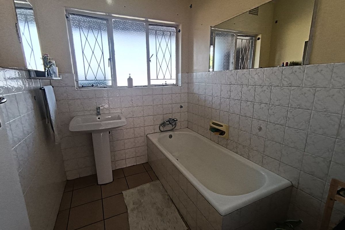 A dated bathroom featuring a pedestal basin, built-in bathtub, and tiled finishes, offering potential for a modern renovation.