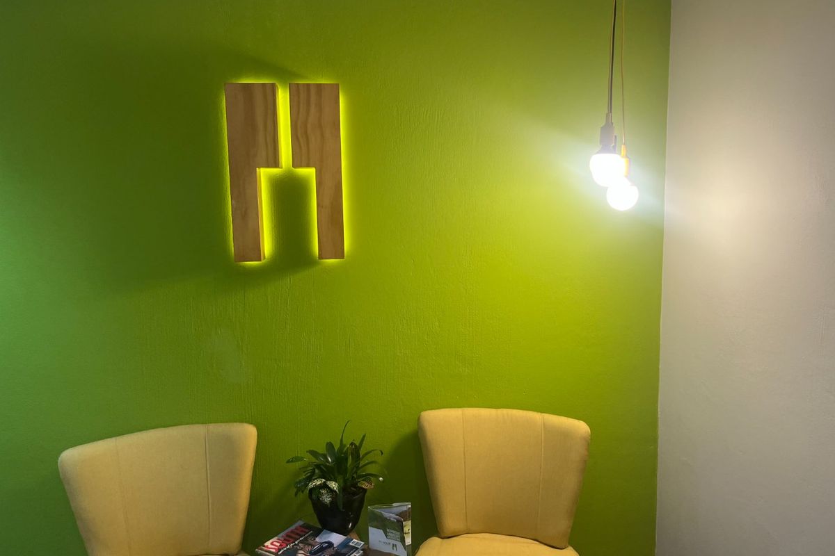A commercial office space featuring a vibrant green accent wall with integrated backlit signage and modern pendant lighting.