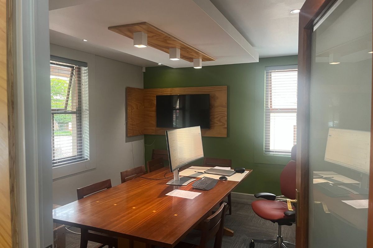 A professional office space featuring a timber feature wall, recessed ceiling lighting, carpeted flooring, and large windows with venetian blinds.