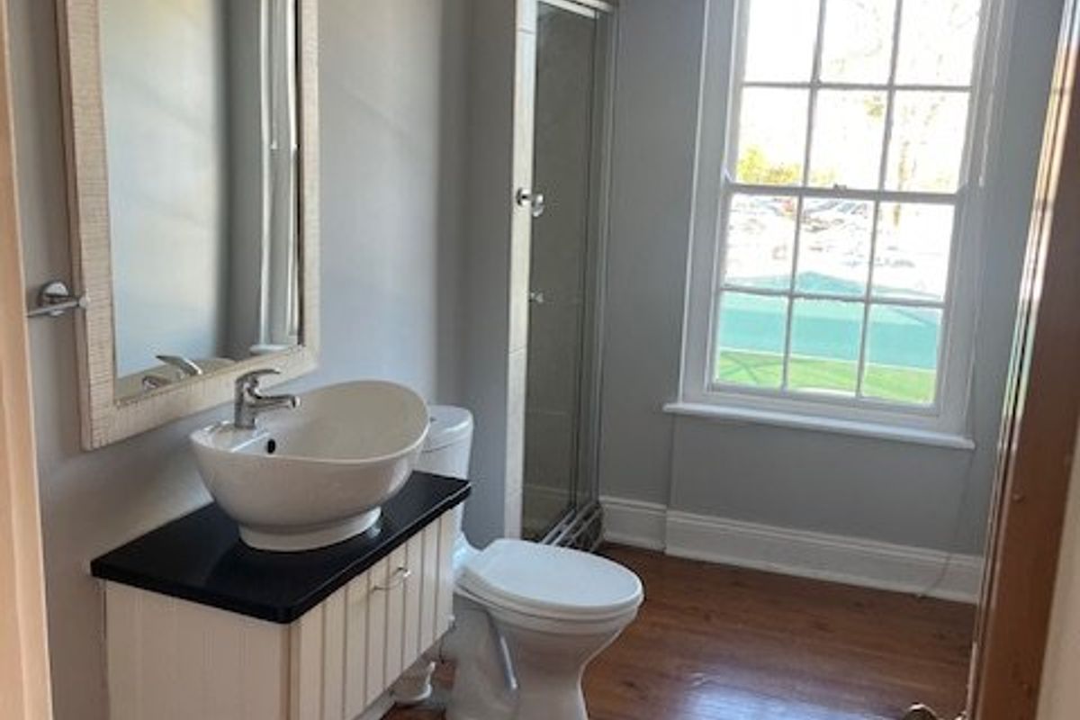 A well-maintained bathroom featuring a vessel sink on a wall-mounted vanity, a toilet, a shower enclosure, and polished timber flooring.