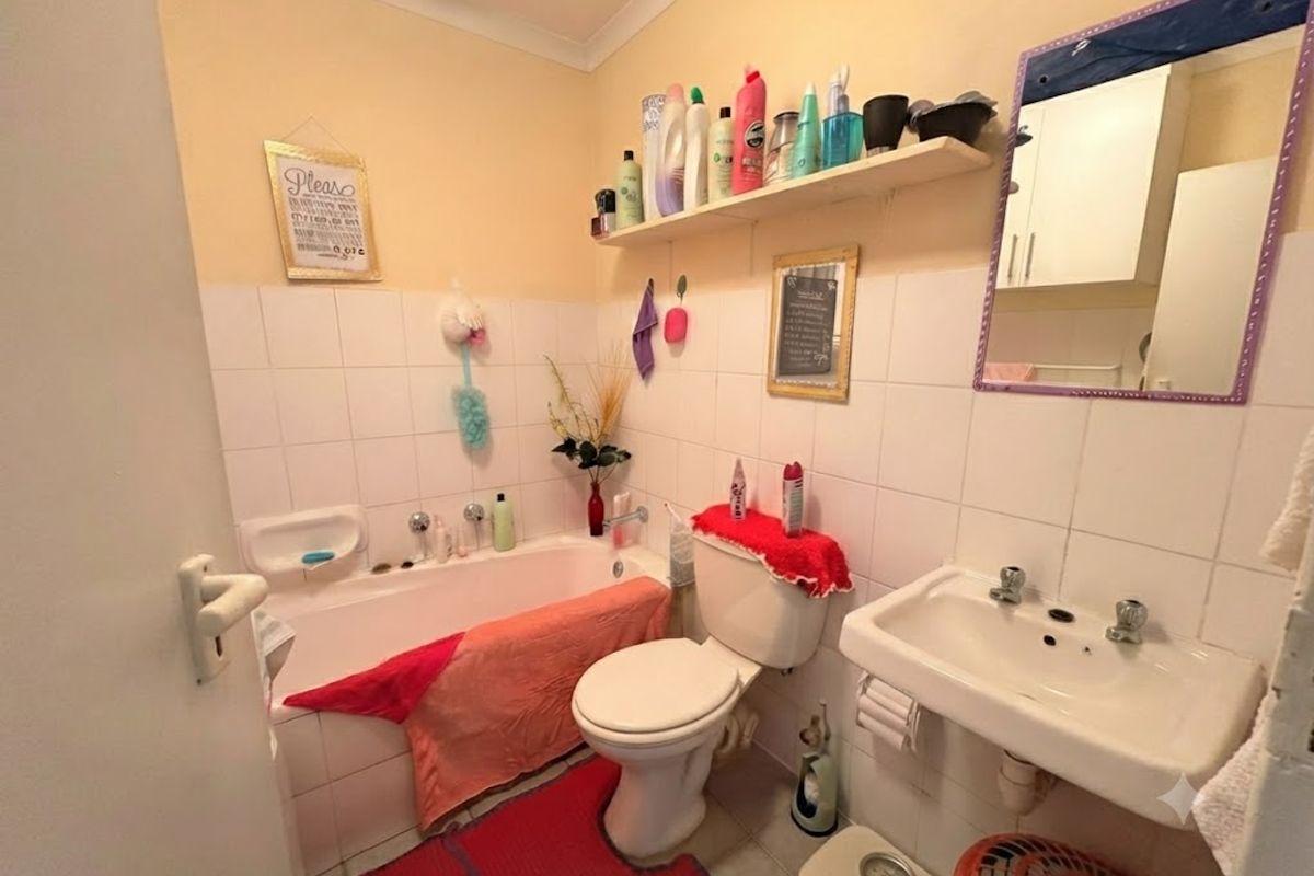 A functional bathroom featuring a bathtub, wall-mounted basin, and toilet with tiled splashbacks and convenient wall-mounted shelving.