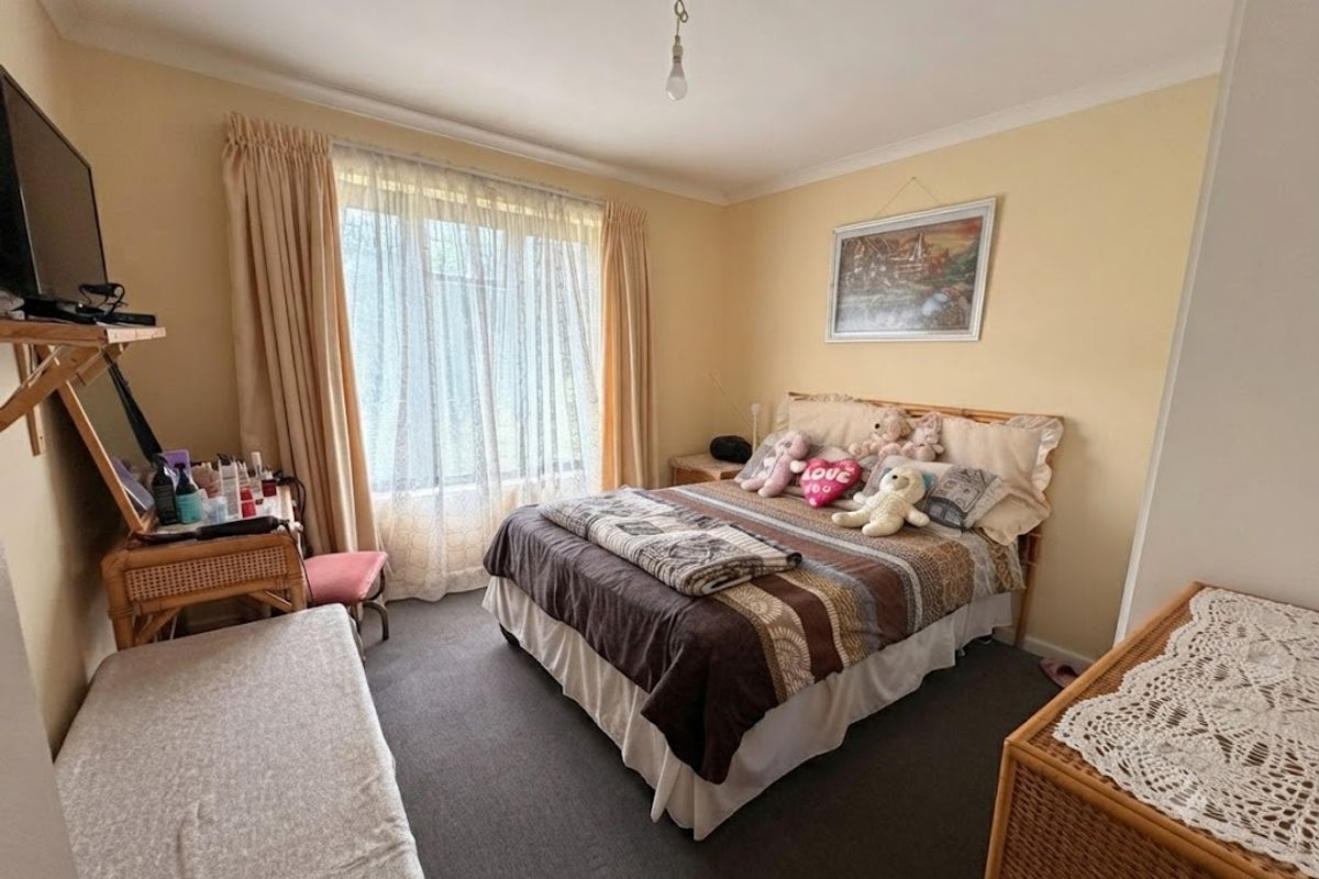 A standard bedroom featuring carpeted flooring, neutral wall paint, and a large window with curtain treatments.