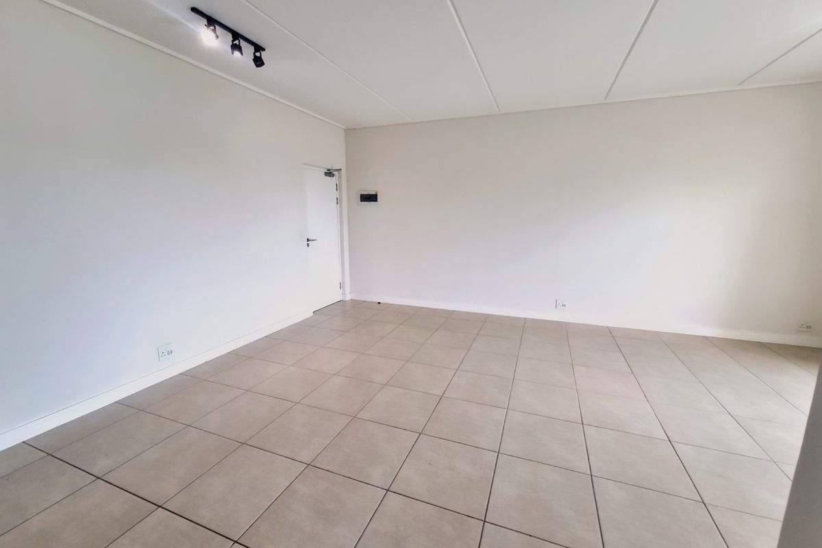 A bright, spacious, and empty living area featuring neutral tiled flooring, clean white walls, and modern track lighting.