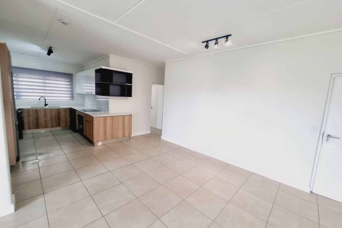 Modern open-plan living area featuring a sleek kitchen with wood-finish cabinetry, integrated appliances, and neutral ceramic floor tiles throughout.