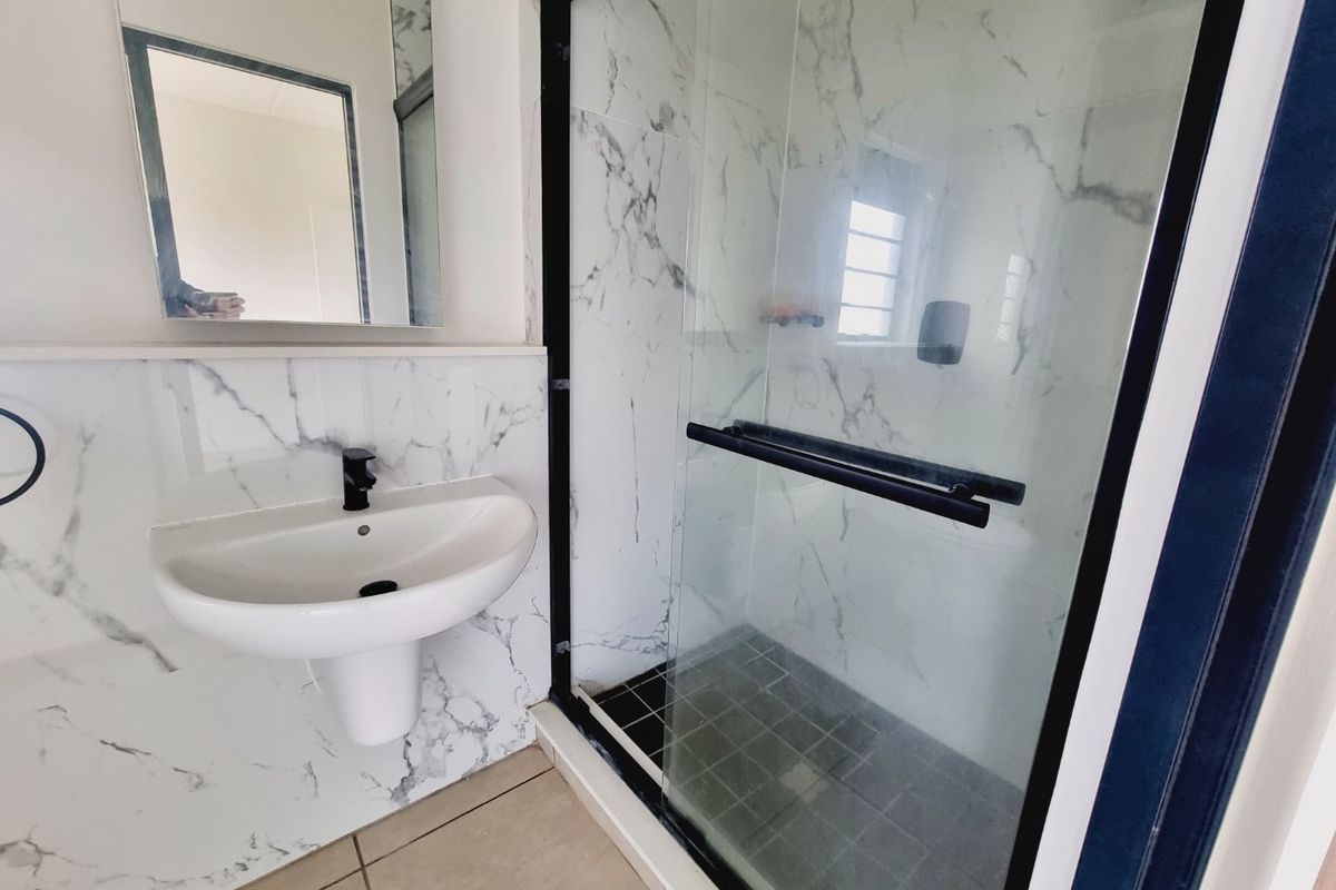 Modern bathroom featuring a pedestal basin with black fixtures, a glass-enclosed shower with marble-look wall tiles, and contemporary finishes.