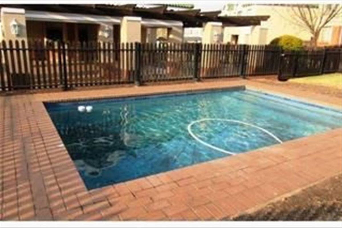 Outdoor pool area featuring a swimming pool with brick paving surround and a timber pergola structure, enclosed by perimeter fencing.