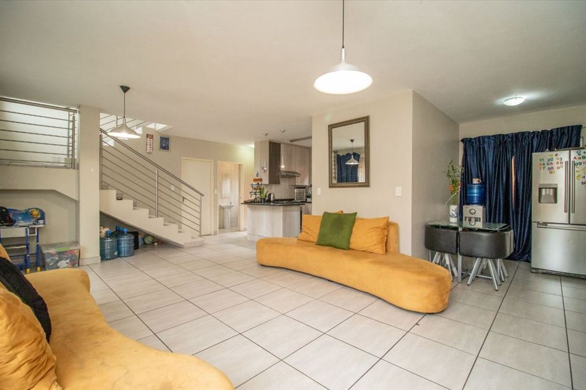 Open-plan living and kitchen area featuring tiled floors, a modern staircase with metal balustrades, and functional kitchen cabinetry.