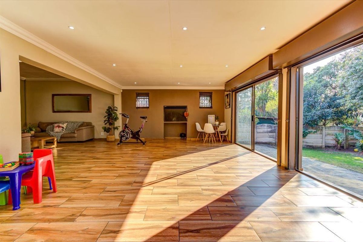 Spacious open-plan living area featuring wood-look tile flooring, recessed lighting, and large sliding glass doors providing seamless access to the garden.