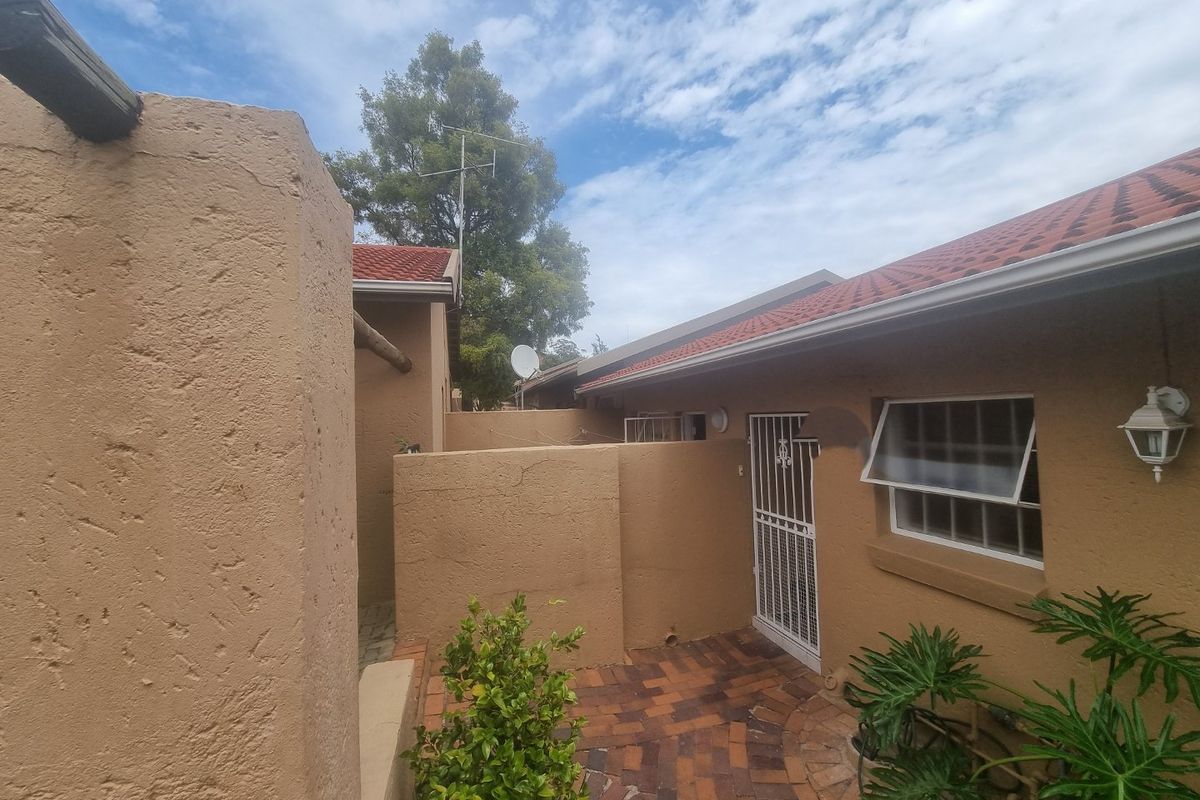 A rear exterior view of the townhouse featuring brick paving, a security gate, and a tiled roof with external wall lighting.