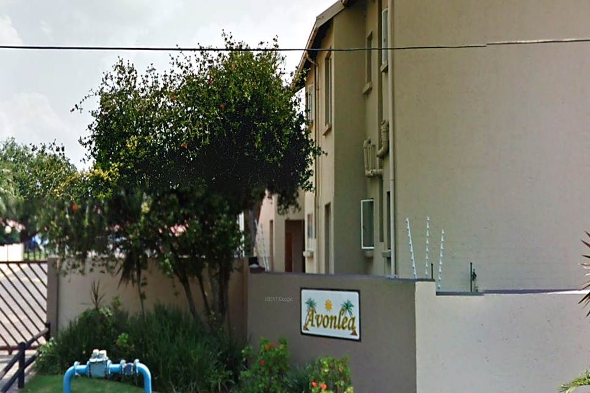 Street view of the Avonlea townhouse complex entrance featuring a boundary wall with electric fencing and complex signage.
