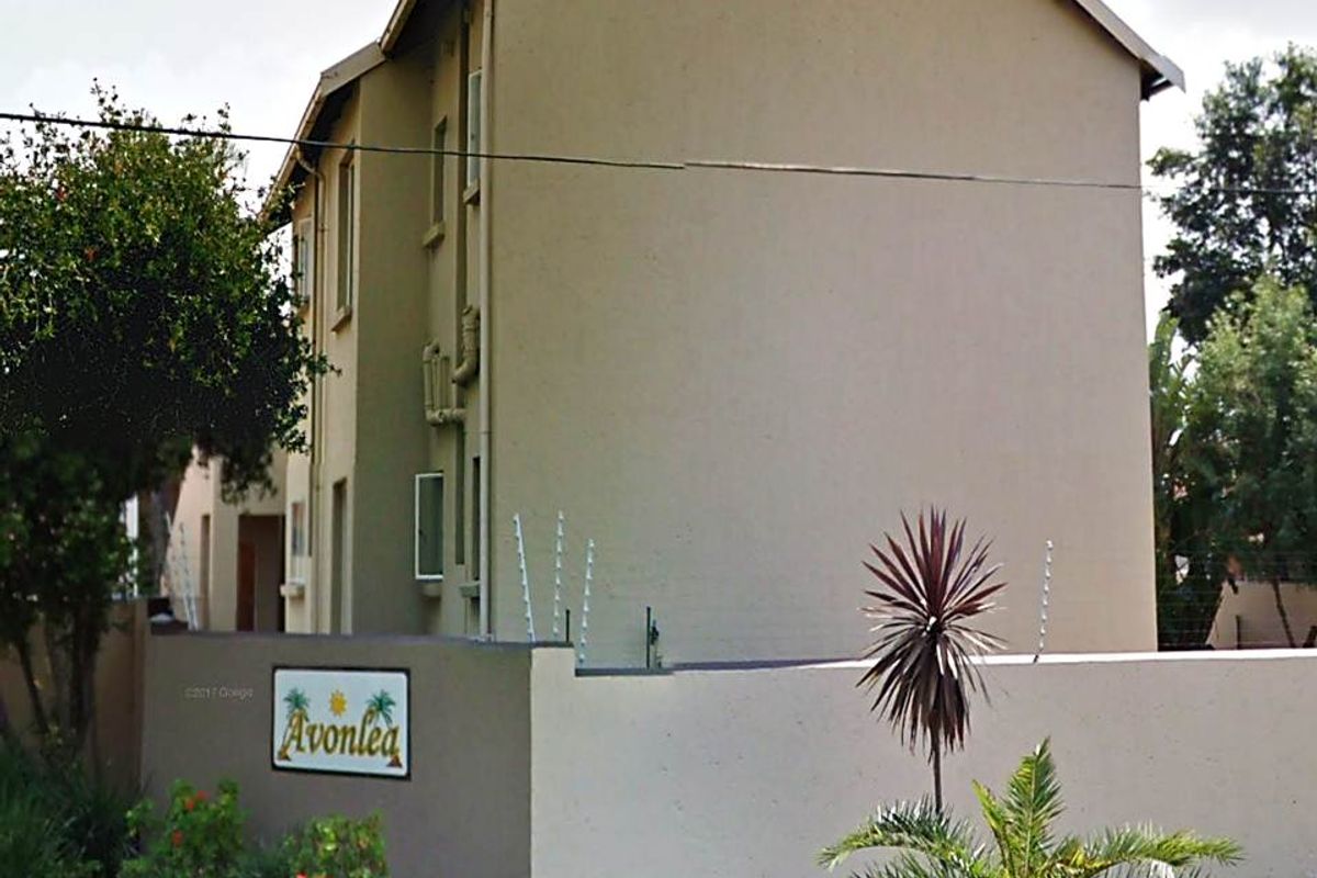 Exterior view of the Avonlea townhouse complex, featuring a perimeter wall with electric fencing and multi-story residential building structure.