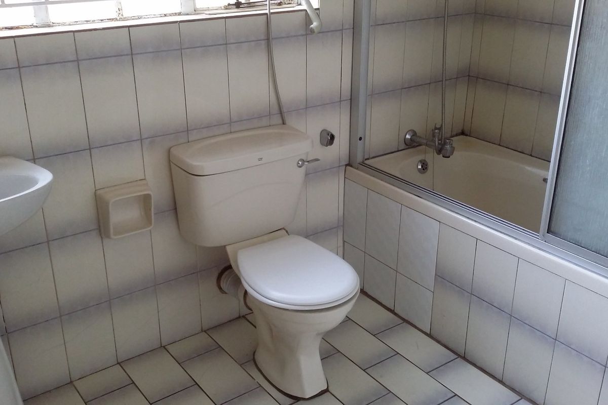 A dated bathroom featuring a pedestal basin, toilet, and a bathtub with a sliding shower screen, finished with original ceramic wall and floor tiles.