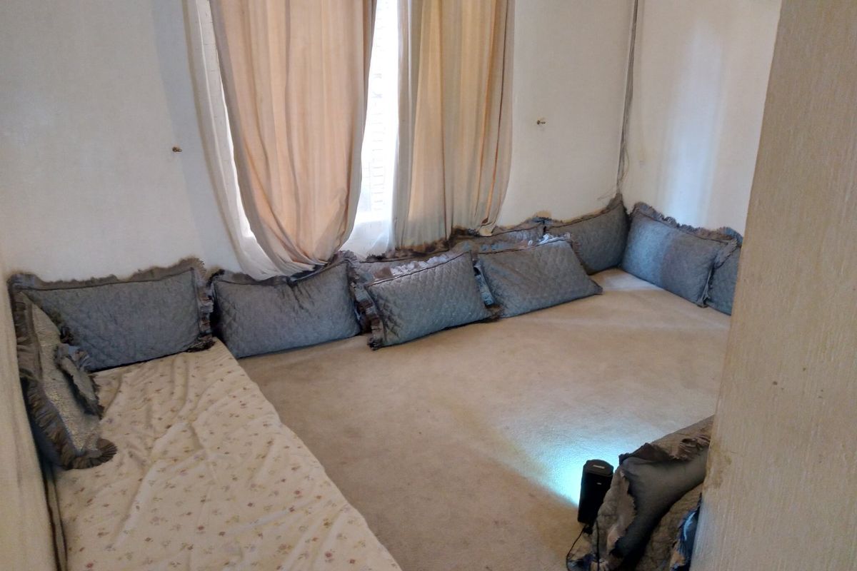 A bedroom featuring carpeted flooring and a window with curtains, currently utilized with floor-level bedding arrangements.
