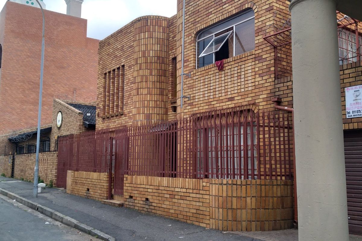Front exterior view of a face brick house featuring metal security fencing and gates along the street boundary.