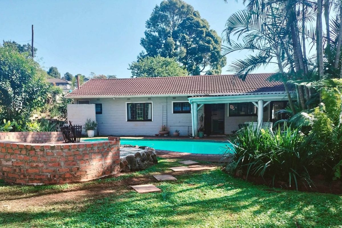 Rear view of the house featuring a swimming pool, a brick fire pit area, and a covered patio space set within a landscaped garden.