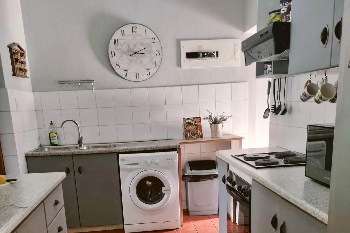 Functional kitchen featuring built-in cabinetry, laminate countertops, electric hob, oven, extractor fan, and tiled splashback with integrated laundry appliance space.
