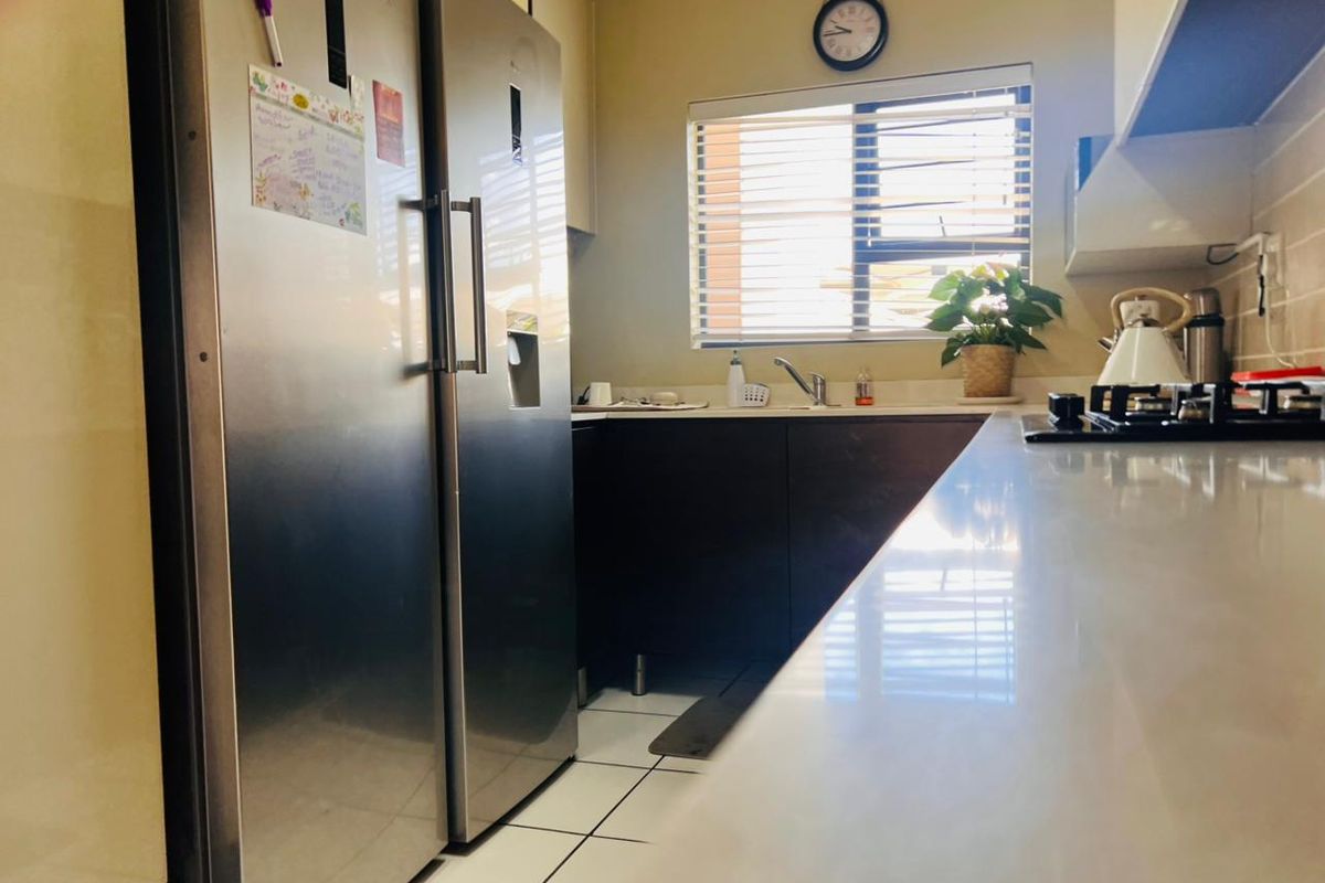 A functional kitchen featuring built-in cabinetry, a gas hob, stainless steel refrigerator, and tiled flooring with natural light from a window.