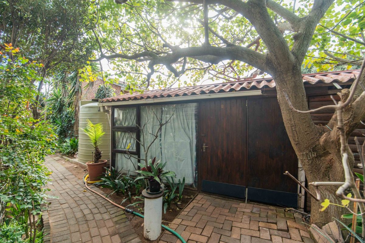 Rear exterior view showing a garden area with brick paving, a water tank, and a structure with timber doors and a tiled roof.