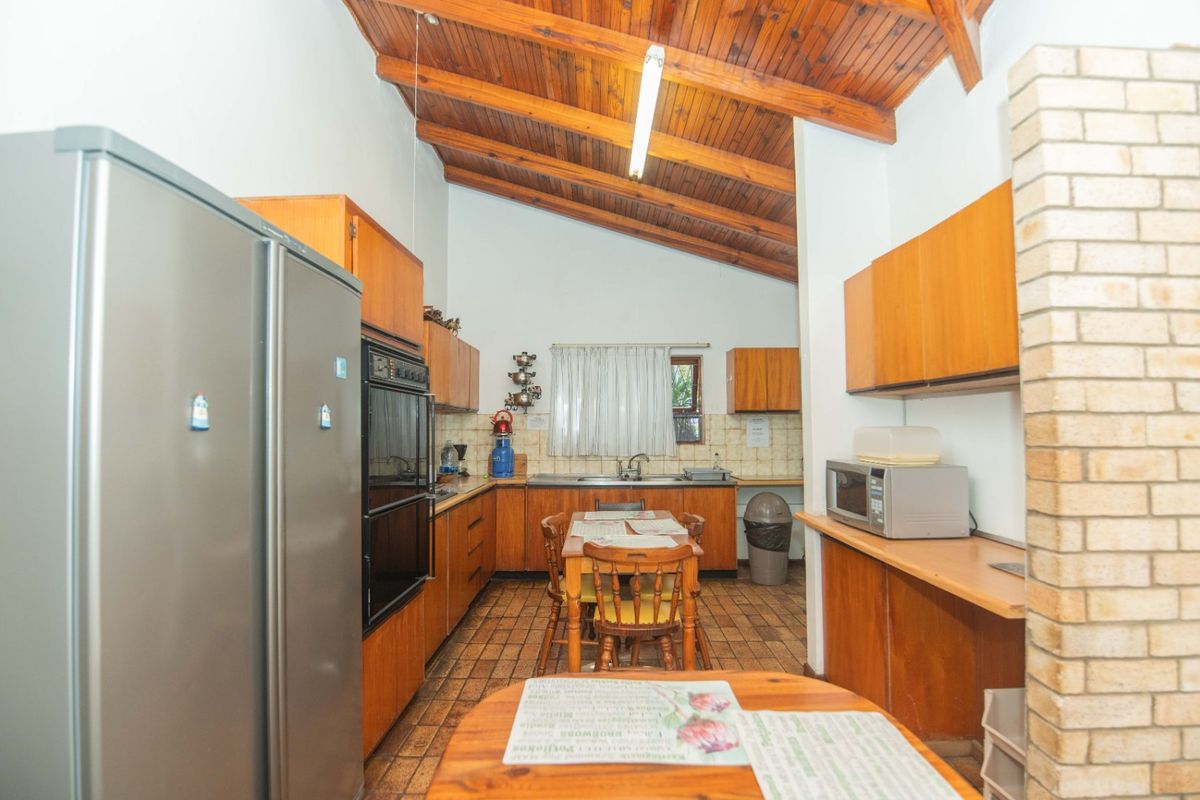 A spacious kitchen featuring wooden cabinetry, exposed timber beam ceilings, tiled flooring, and a distinctive brick feature pillar.